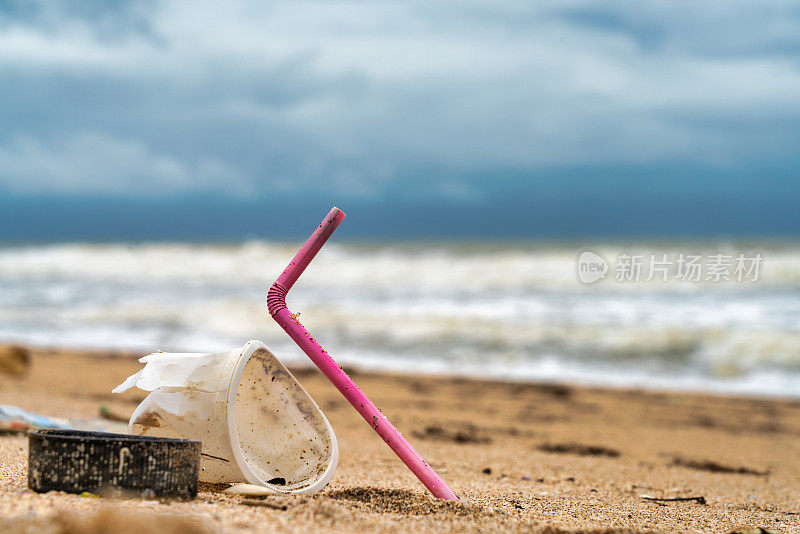 粉红色的吸管和塑料杯被扔在海滩上