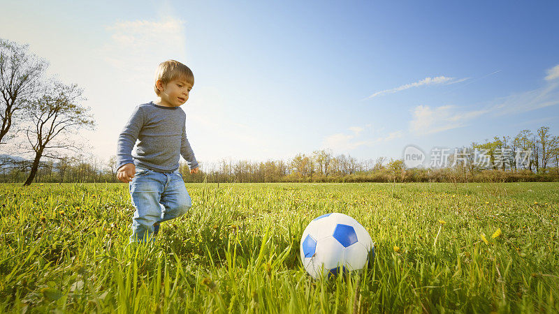 男孩在阳光明媚的草地上踢足球
