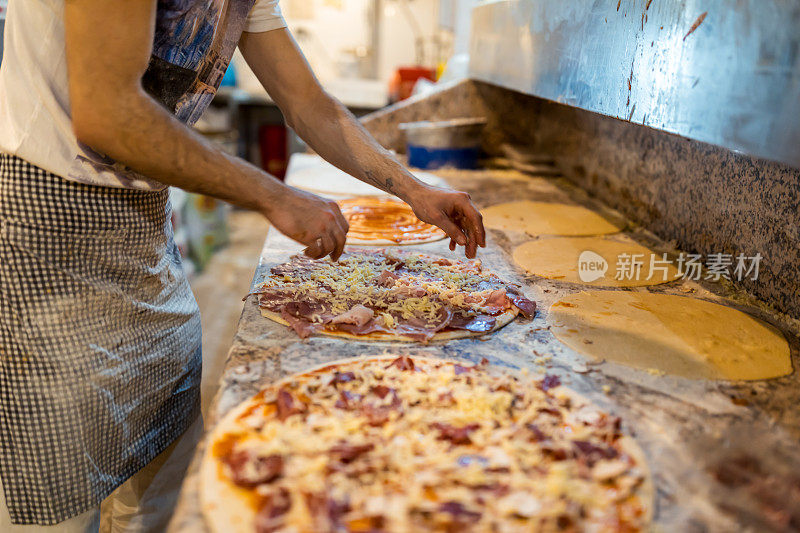 特写厨师的手，面包师在厨房做披萨。制作披萨的过程。双手准备披萨。