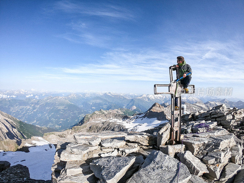 登山者坐在山顶的十字架上凝视着山顶的景色