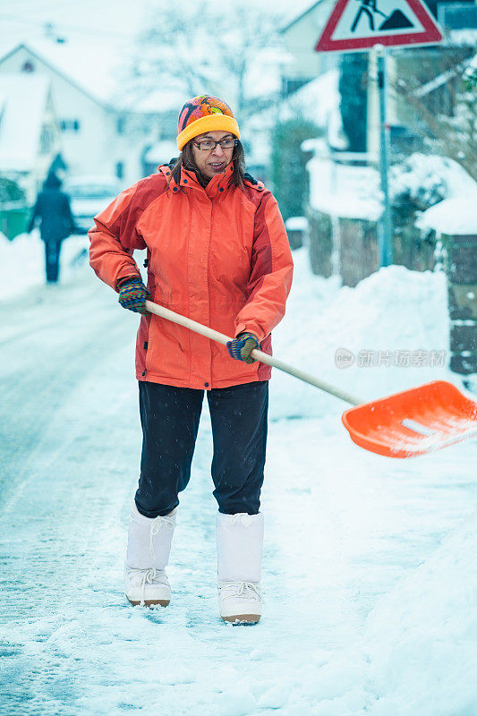 一个成熟的女人在清扫屋前的积雪