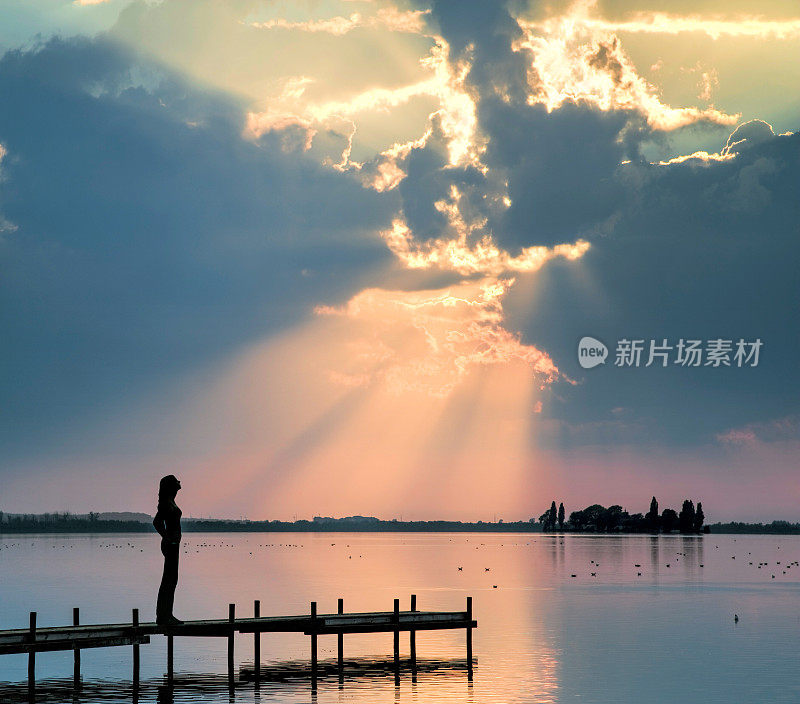 女人的剪影在湖边防波堤上观看雄伟的云景