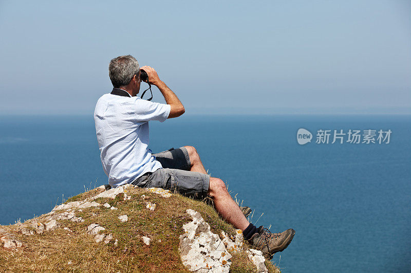 一个成熟的白人男人坐在悬崖顶上用望远镜看东西