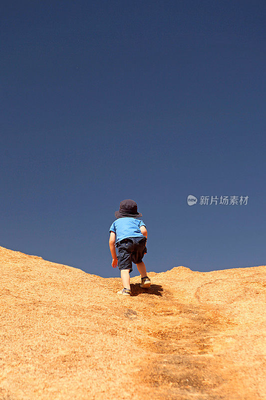 在蓝天背景下，孩子爬岩石山