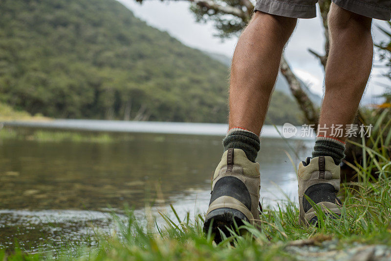 男人的腿和远足站在一个山湖边