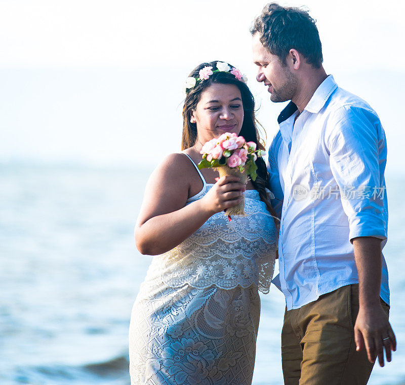 一对年轻的新婚夫妇在阳光明媚的海滩上相爱