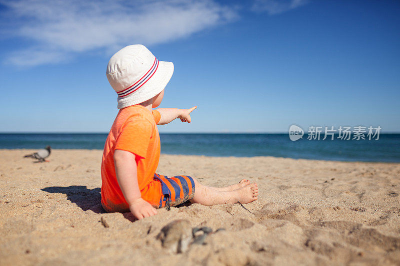 小男孩坐在海滩上，指着大海