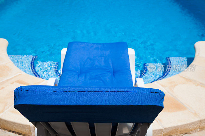 阳光躺椅在美丽的阳光明媚的蓝色游泳池