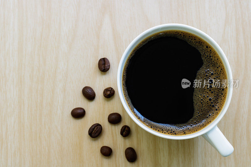 木桌上的咖啡杯和咖啡豆。黑咖啡，白色陶瓷杯，近，顶视图。