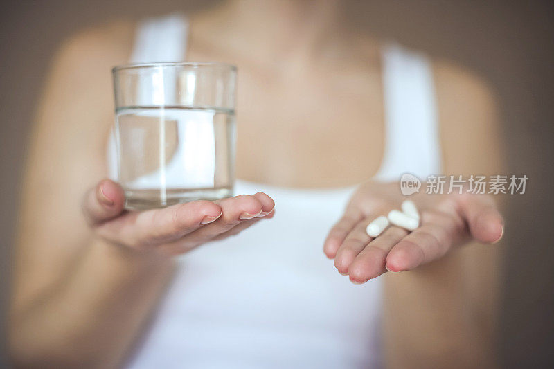 女人拿着一杯水和药丸。注意力集中在手上。