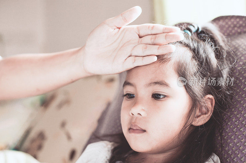 可爱的亚洲儿童女孩的疾病和母亲的手触摸她的额头，以爱和照顾检查温度