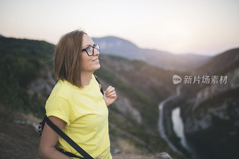 一个背着背包的年轻女子站在山顶上欣赏日落。