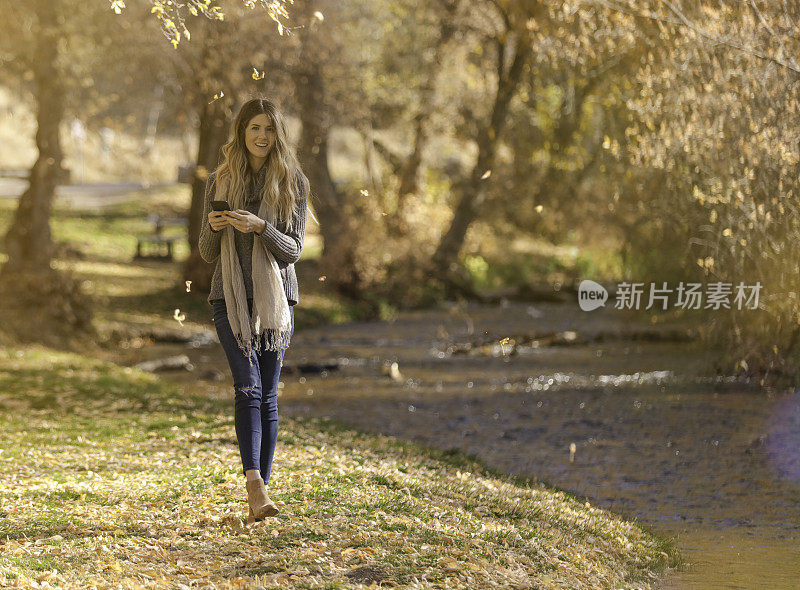 女人秋天在公园散步，带着手机