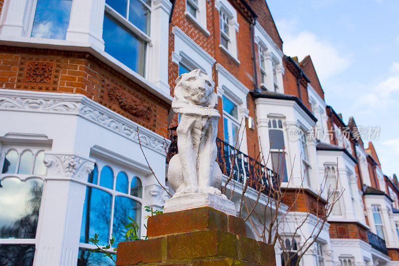 在英国伦敦的一条当地街道上，一排翻新的维多利亚风格的红砖白墙豪宅前，白色石雕的狮子雕像