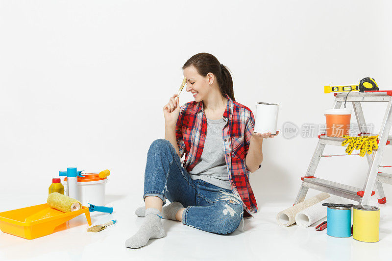 女人坐在地板上用刷子、油漆罐、仪器进行装修，房间隔离在白色的背景上。墙纸，胶水配件，油漆工具。修理家里的概念。本空间