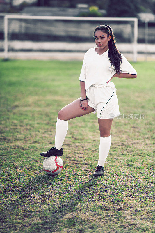 可爱的女足球运动员摆姿势与脚上的球