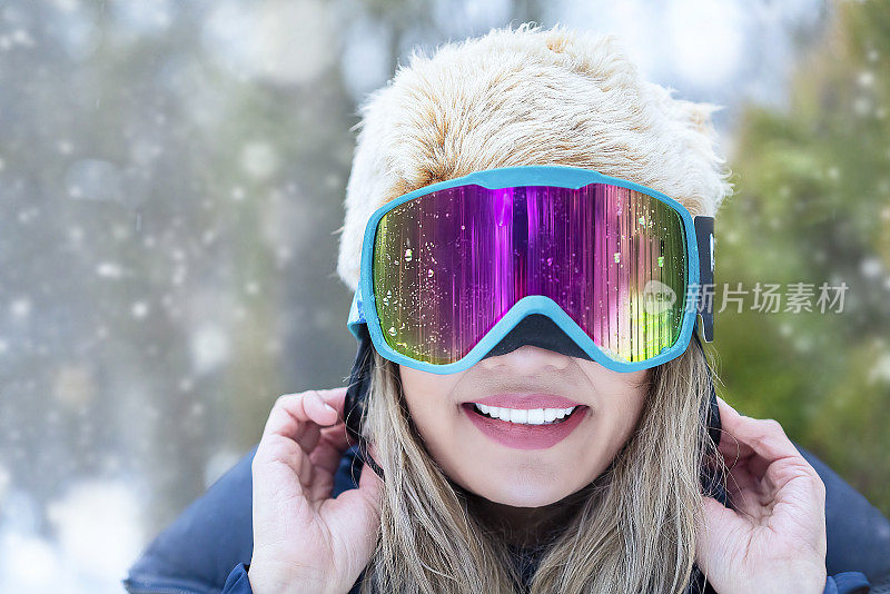 女滑雪板运动员的肖像与滑雪镜看着相机和微笑