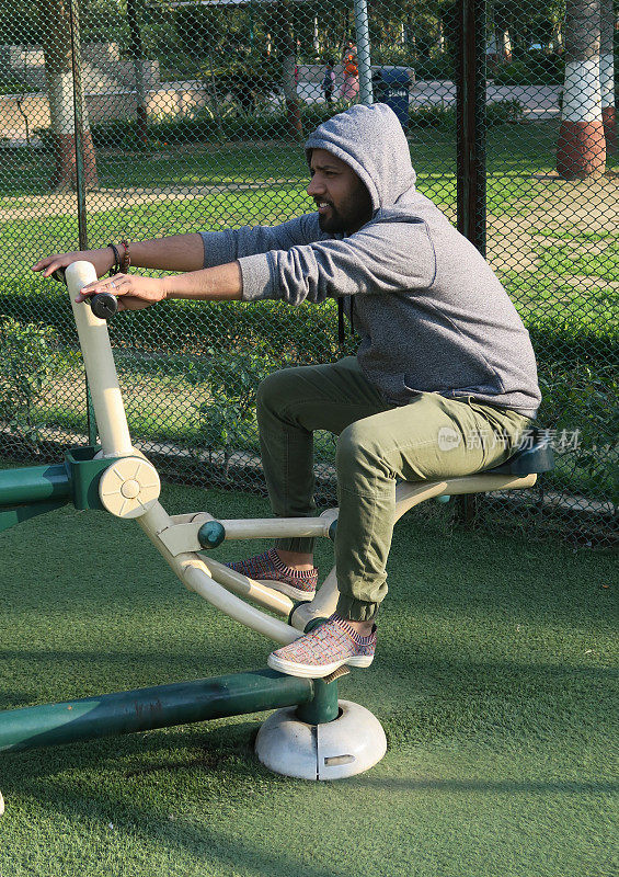 印度男子在户外健身房里使用Rider健身器材，在露天公园里锻炼
