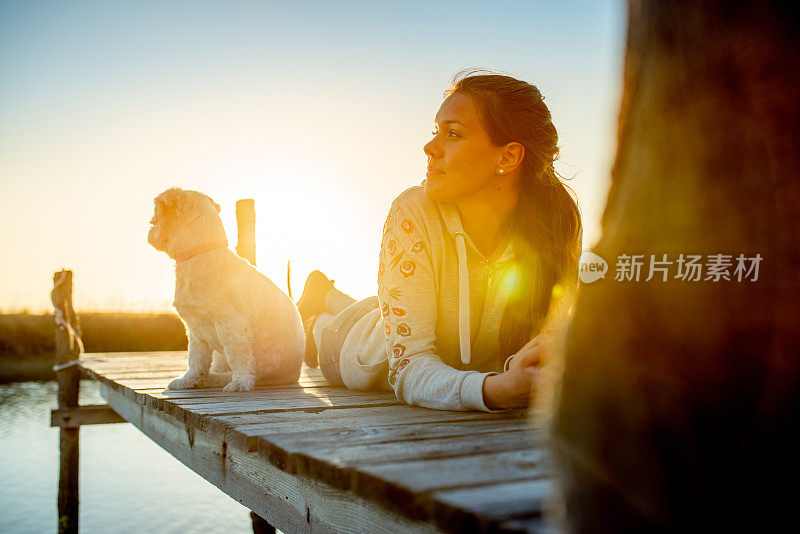 年轻女子放松与她的狗在户外日落