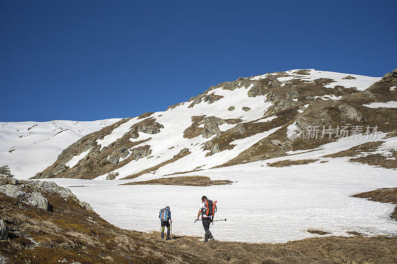两个徒步旅行者在雪山上行走，荒野地区