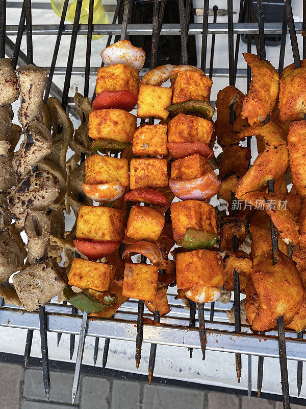 鸡肉和蔬菜串显示在金属架单元，鸡胸肉片炭火烤，串洋葱和红青椒覆盖在辣酱在大排档，提高的观点