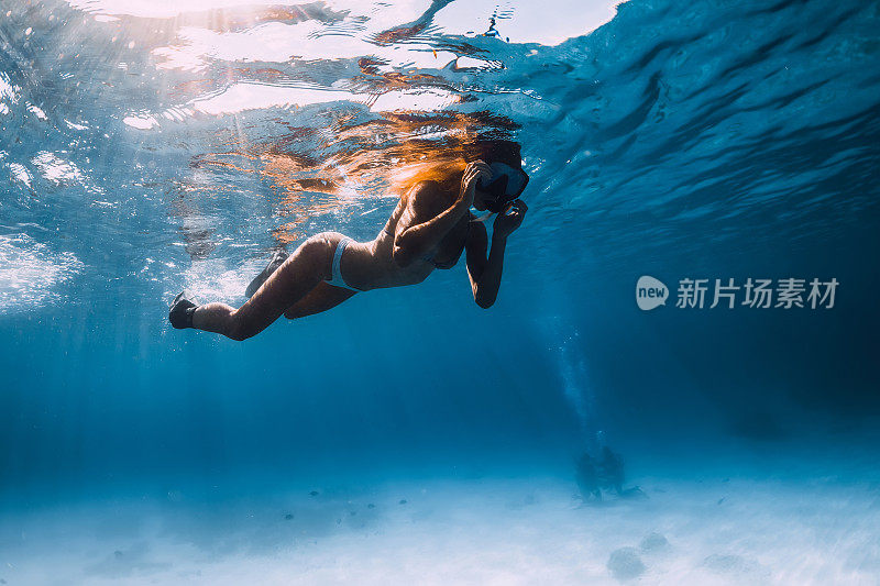 年轻女子带着脚蹼和面具在蓝色的海洋里游泳。水下视图