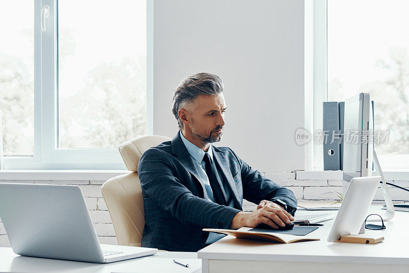一个穿着正装、自信成熟的男人坐在工作的地方使用电脑