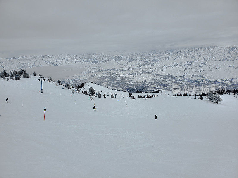 犹他州雪盆滑雪场的滑雪者在多云的平坦光线下在一个碗里高高地滑雪。