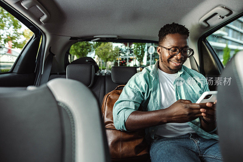 一名年轻男子在出租车后座使用智能手机