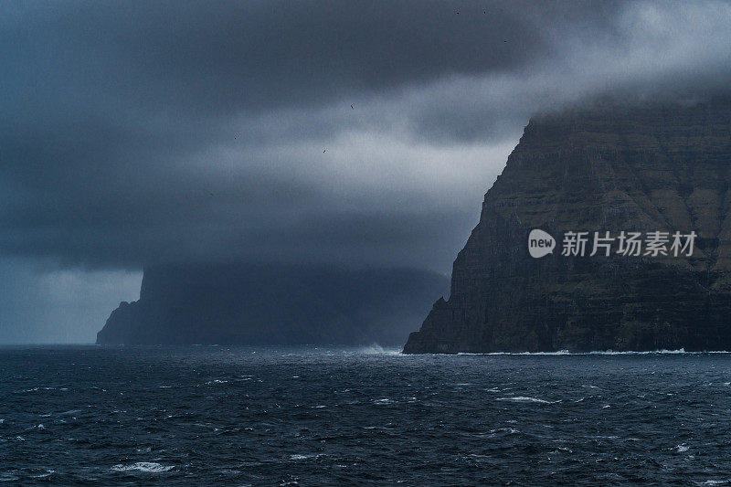 法罗群岛的海景从渡轮在波浪的水域。暴风雨天气，有很大的云景和一些阳光。