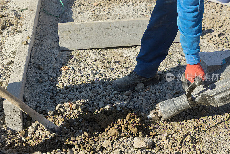 在施工道路上，工人们用手提钻在混凝土表面上钻孔和挖掘。