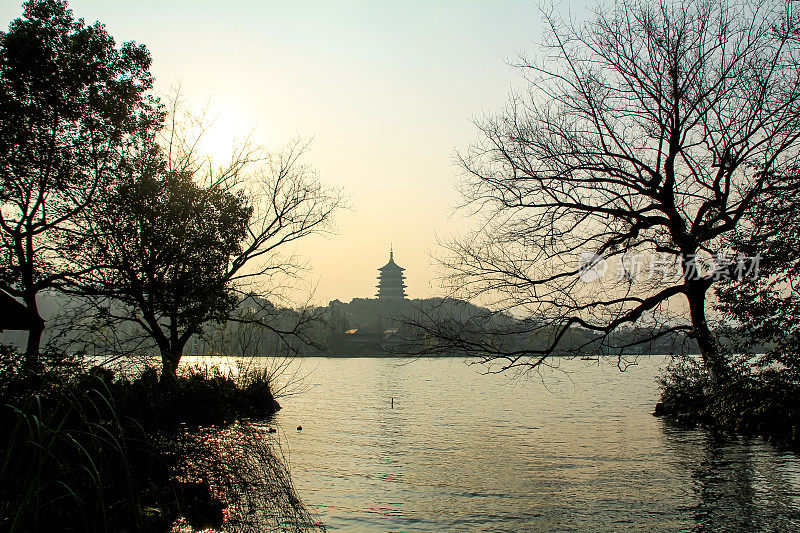 以树木为前景的宁静海景。日落时平静的海景，背景是群山和一座中国寺庙。