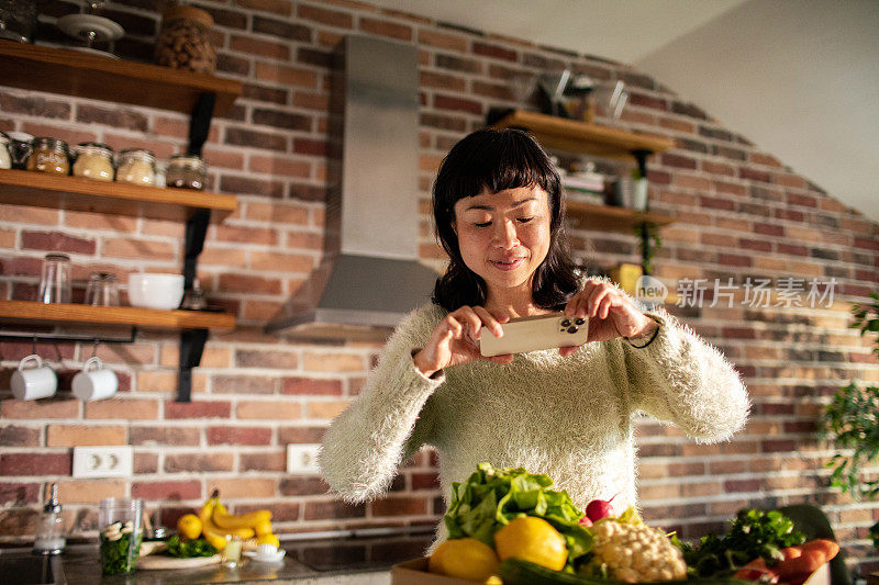 一名年轻的日本女子用智能手机拍下了装满水果和蔬菜的盒子