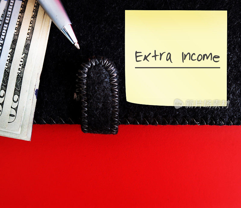 笔和美元钞票现金钱在黑色笔记本上，备注写额外收入，在红色背景与复制空间。从兼职、副业、第二份工作中获得更多收入的概念