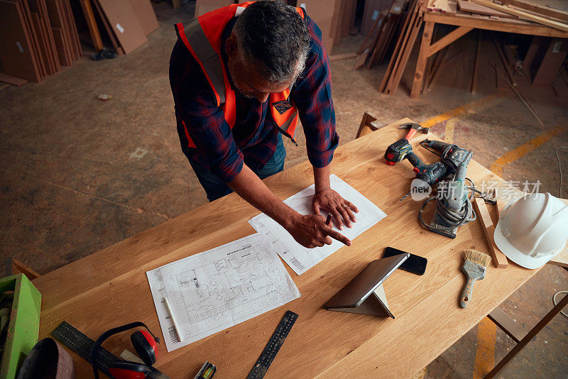 木工工厂里，中年男子在数码平板电脑和工具旁边指指点点
