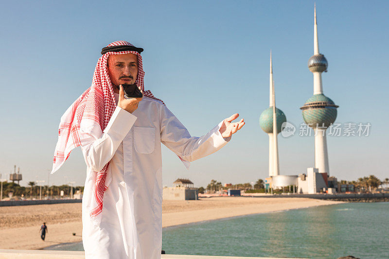 年轻的酋长正在打电话，背景是科威特的塔楼