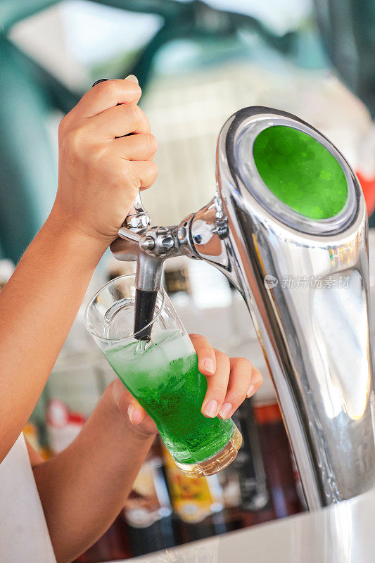 在圣帕特里克节的庆祝活动中，酒吧里的酒保把绿色啤酒倒进玻璃杯里