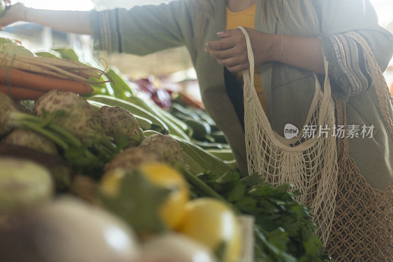 一个不知名的女人在农贸市场上挑选新鲜蔬菜，把它放在一个可重复使用的网袋里