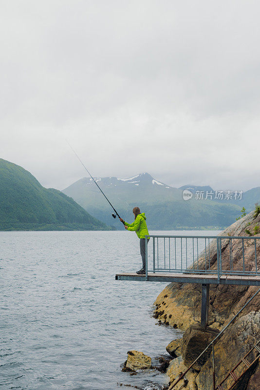 身穿绿夹克的女子在挪威峡湾钓鱼