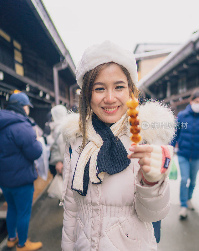 美丽的女游客在雪天的日本之旅中品尝日本街头小吃。