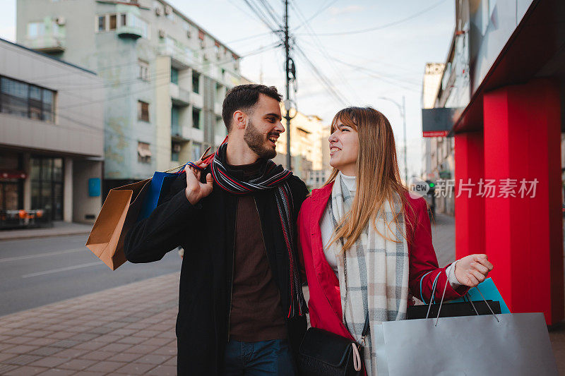 幸福的年轻夫妇拎着购物袋在城市里漫步