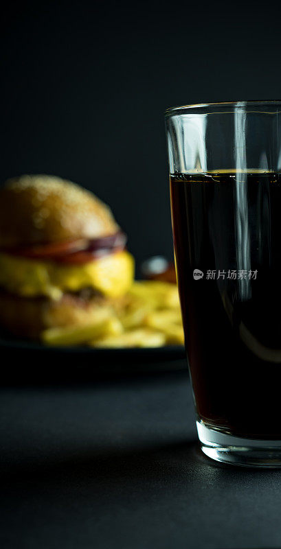 一杯可乐靠近模糊的汉堡和薯条在黑色的背景