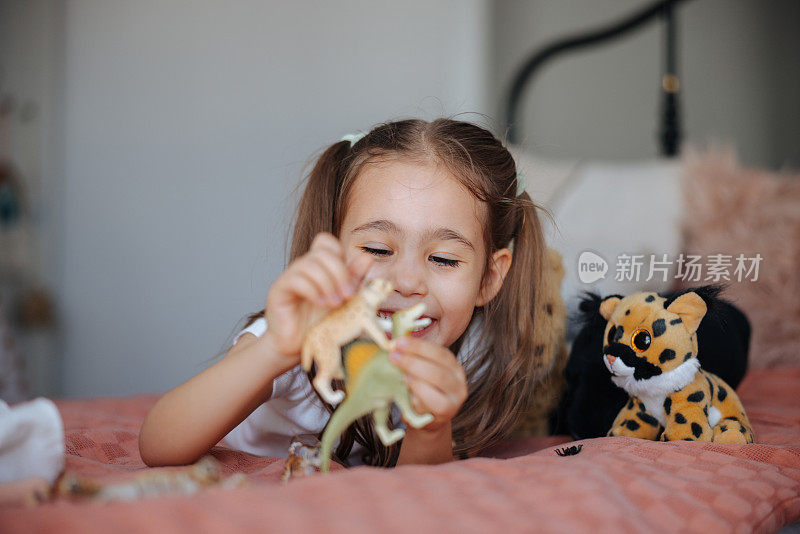 活泼可爱的孩子在卧室里玩塑料恐龙玩具。活泼可爱的孩子在卧室里玩塑料恐龙玩具。