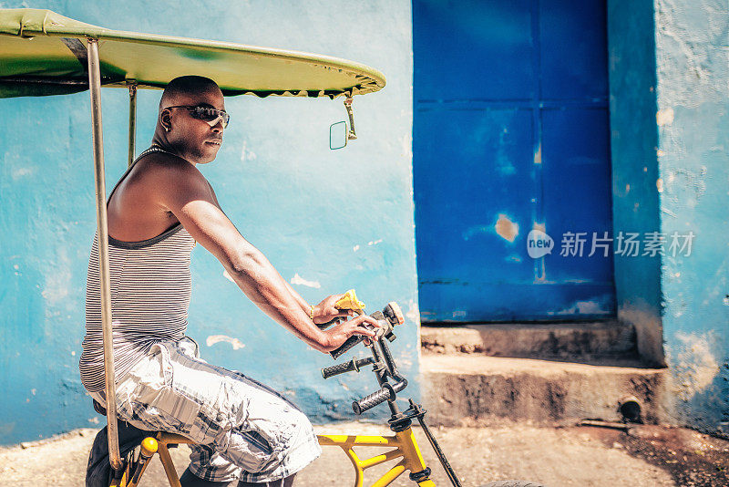 蓝色墙前的古巴自行车出租车司机