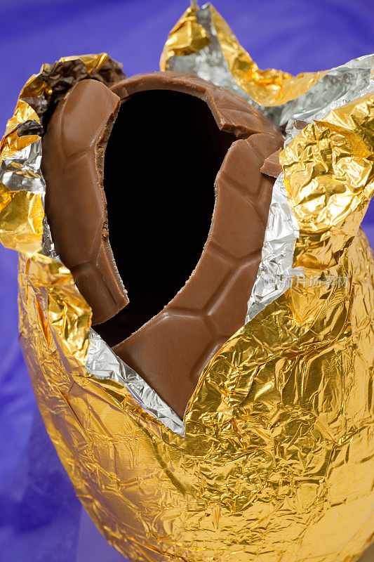 拆开的巧克力复活节彩蛋在金箔上涂上紫色