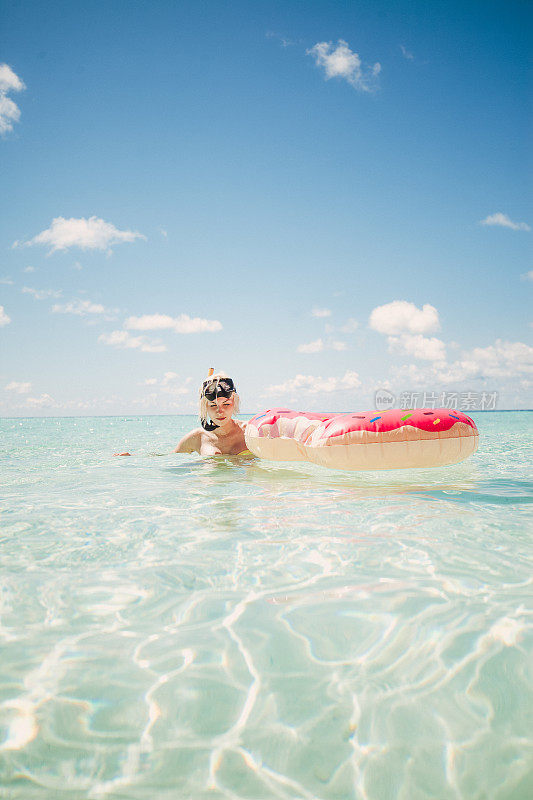 一名金发女子站在马尔代夫的浅水里，手里拿着通气管