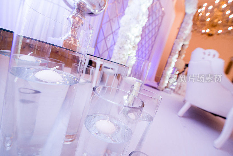 白色婚礼舞台上的大玻璃花瓶上漂浮着蜡烛