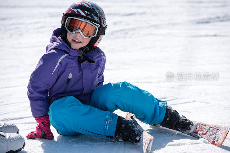 穿着滑雪服的女孩坐在雪地上