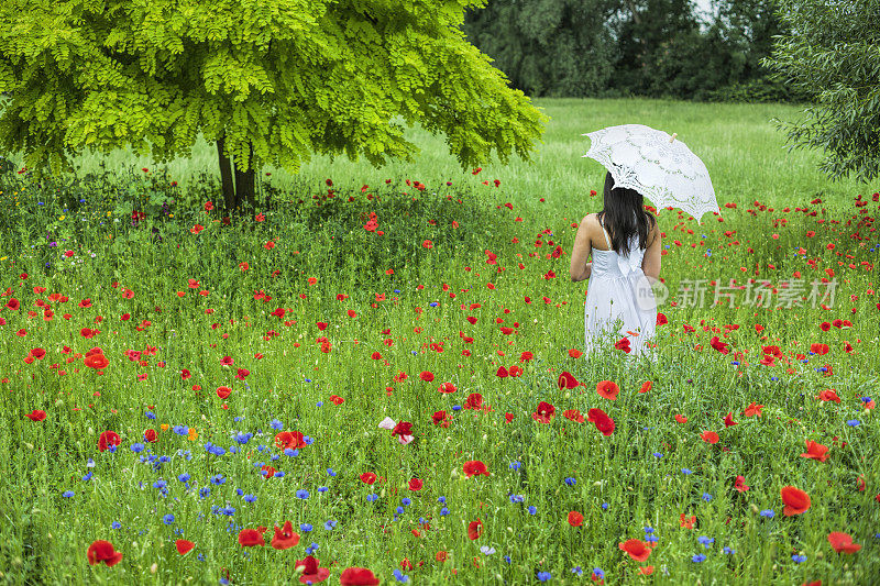 年轻女子在花园里穿着白色的太阳裙和雨伞