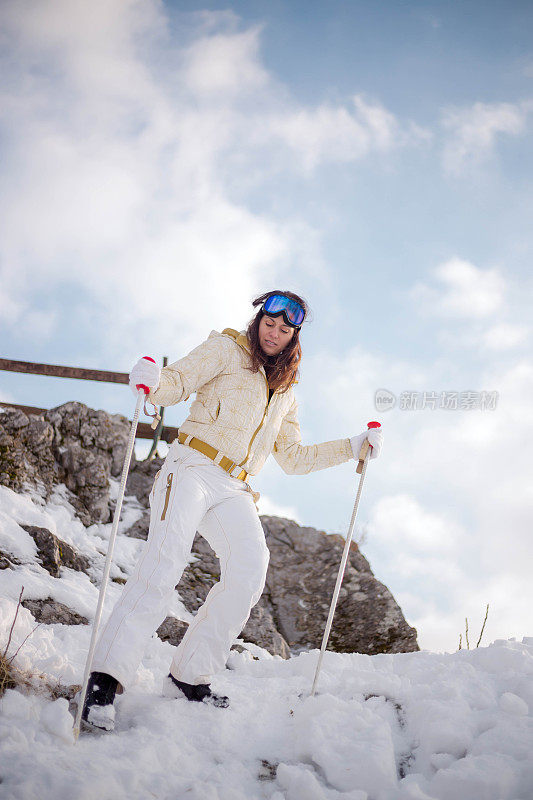 近景美丽的年轻女子在冬天的衣服站在一边，手拿木棍的背景雪山